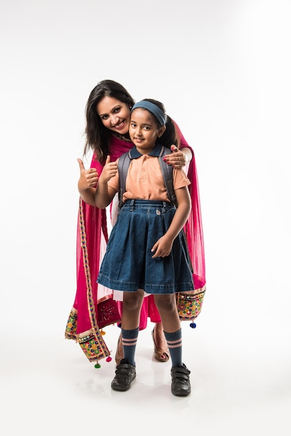 Madre india ayudando a la niña de la escuela con uniforme preparándose con lonchera, peinado o esperando el autobús escolar