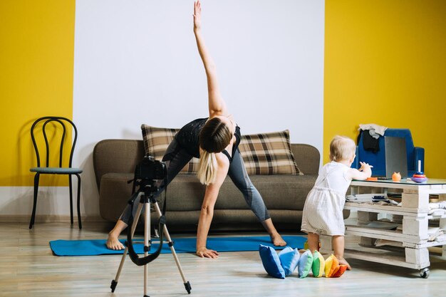 Foto madre instructora de fitness entrenador personal grabar video cerca de la cámara en casa con su hija