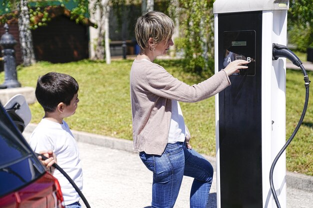 Foto una madre instruye alegremente a su hijo sobre la carga de vehículos eléctricos en un día radiante