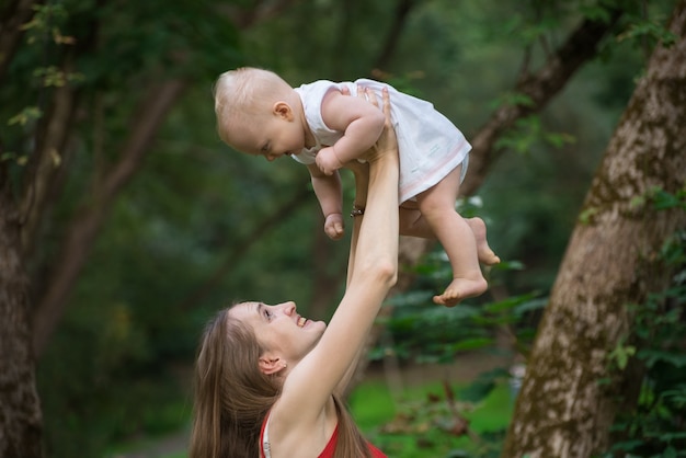 La madre joven alegre levanta al bebé en sus brazos. Feliz maternidad e infancia.