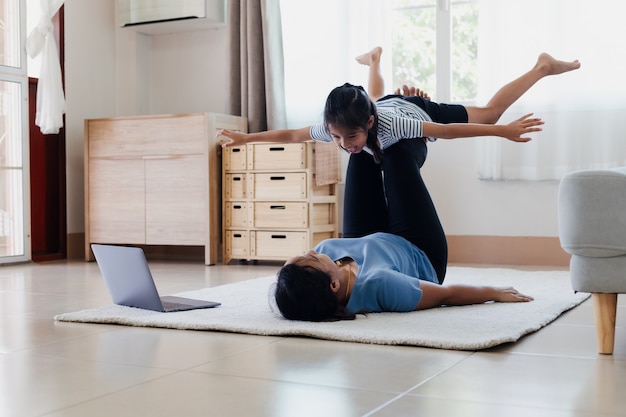 Madre joven asiática y su hija que hacen yoga del ejercicio de la aptitud del estiramiento juntos en casa. Los padres que enseñan a sus hijos a ejercitarse para ser fuertes y mantener la salud física y el bienestar en la rutina diaria.