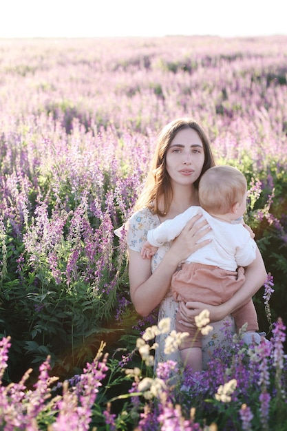 Una madre joven con un bebé en un campo brillante y floreciente