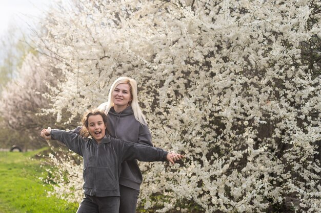 Madre joven e hija juntas, abrazándose y riéndose alegremente mientras se relajan en las flores de primavera durante unas vacaciones. Estilo de vida familiar al aire libre.