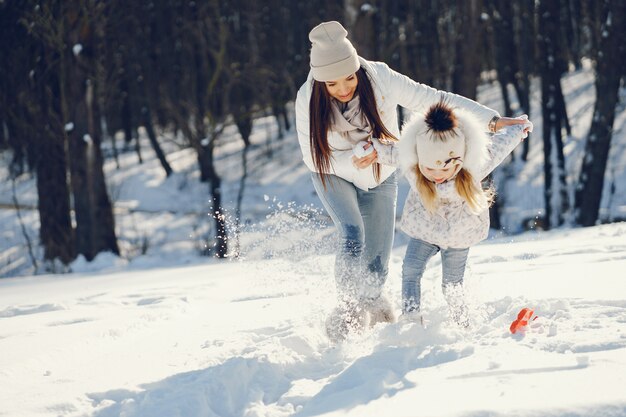 madre joven y elegante jugando con su pequeña hija linda en el parque de nieve de invierno