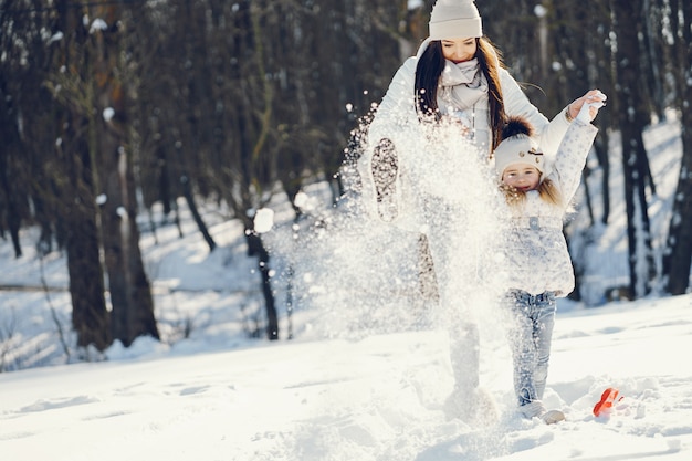 madre joven y elegante jugando con su pequeña hija linda en el parque de nieve de invierno