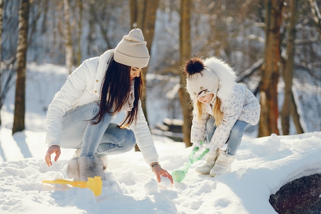 madre joven y elegante jugando con su pequeña hija linda en el parque de nieve de invierno