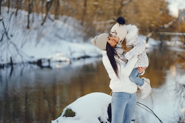 madre joven y elegante jugando con su pequeña hija linda en el parque de nieve de invierno