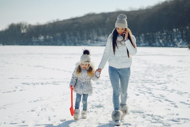 madre joven y elegante jugando con su pequeña hija linda en el parque de nieve de invierno