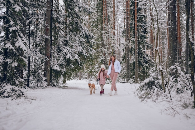 Madre joven de familia feliz y niña linda en ropa de abrigo rosa caminando divirtiéndose con el perro rojo shiba inu en el bosque de invierno frío blanco como la nieve al aire libre