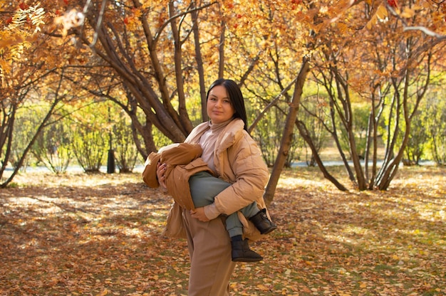 Una madre joven y feliz con un niño en un parque de otoño. Mamá abraza y besa a su hijo en la calle. Temporada de otoño, el concepto de crianza e hijos.