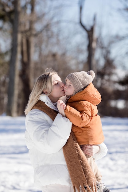 Madre joven feliz con su hijo caminando en el parque de invierno Retrato de familia feliz al aire libre Niño arrojando nieve a la madre