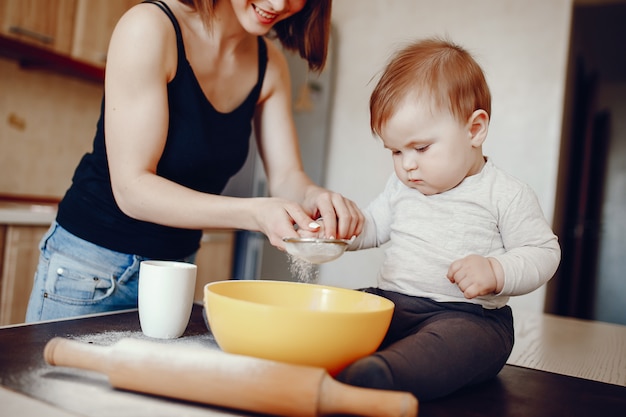 Una madre joven y hermosa está preparando la comida en la cocina, junto con su pequeño hijo