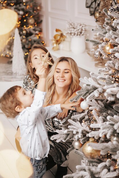 Una madre joven y hermosa y sus hijos están decorando un árbol de Navidad