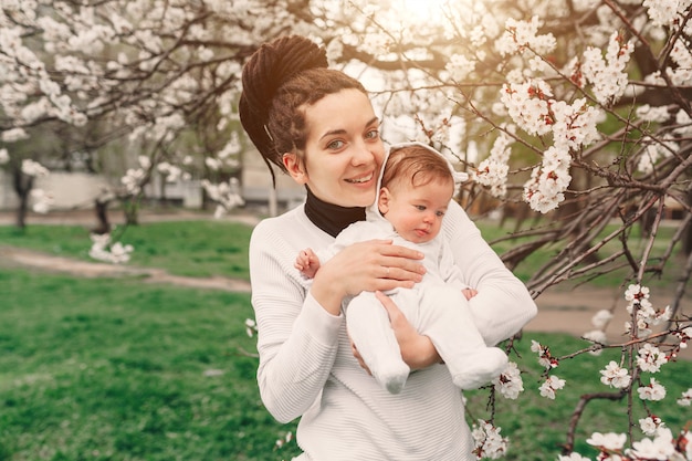 Madre joven con la hija adorable en parque con el árbol del flor. Feliz madre e hijo