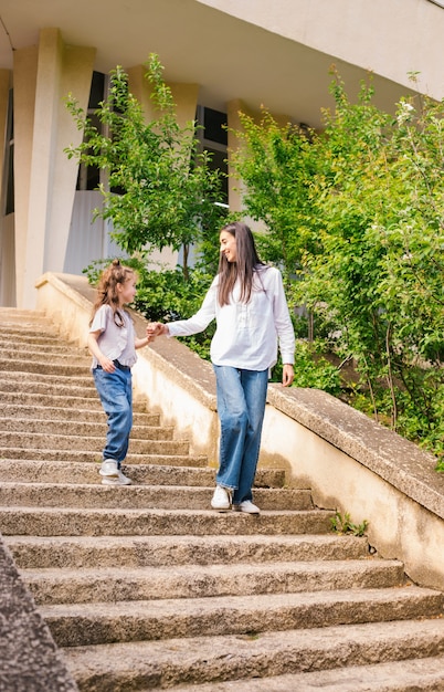 Una madre joven con una hija pequeña baja las escaleras. Una mujer toma la mano de una niña y le habla.