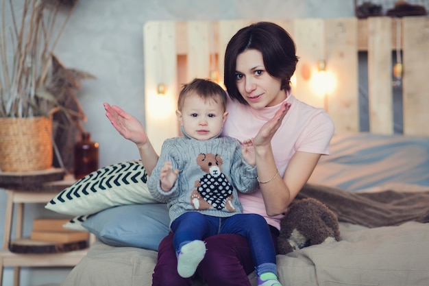 Madre joven jugando con su niña en el dormitorio