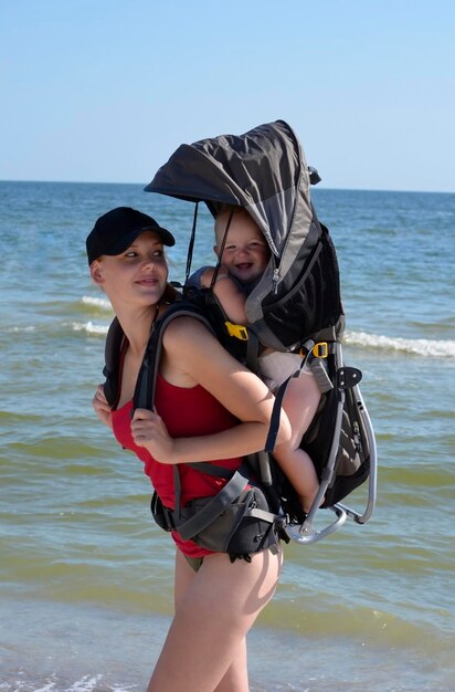 Una madre joven con un niño pequeño en una bolsa de transporte detrás de su espalda