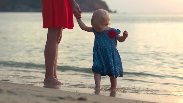 Madre joven y pequeña hija jugando con arena y olas de mar en la playa