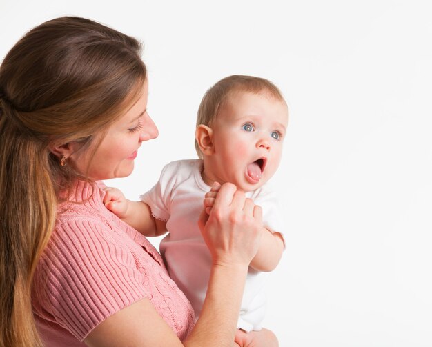 Madre joven positiva tiene en sus manos una encantadora hijita mostrando la lengua en un blanco