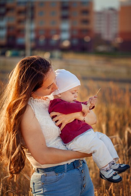 Madre joven con su niño lindo, disfrutando del día soleado sobre campo del verano.