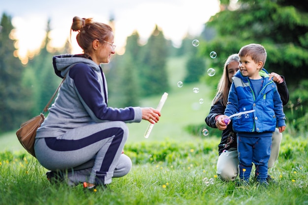 Madre juega con hija e hijo en pompas de jabón en un bosque durante un paseo