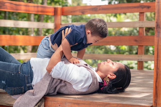 Una madre juega en el suelo con su hijo con síndrome de Down y lo levanta con los brazos.