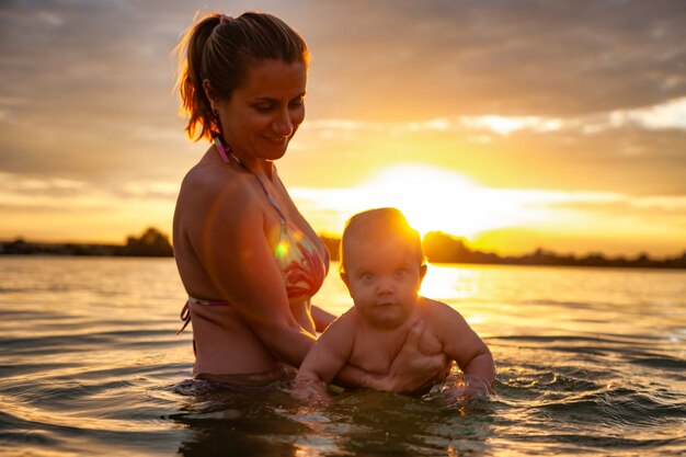 Madre jugando con el bebé en el agua durante la puesta de sol.