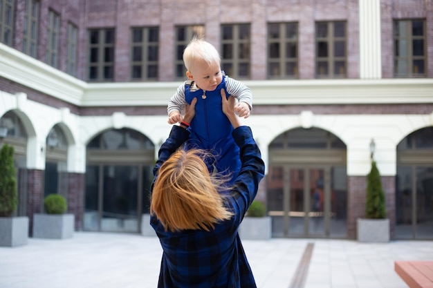 Madre jugando con un niño con ropa elegante al aire libre en el fondo urbano