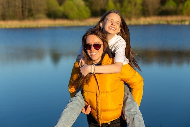 Madre juguetona dando a su hija un paseo a cuestas en la orilla del lago Spring