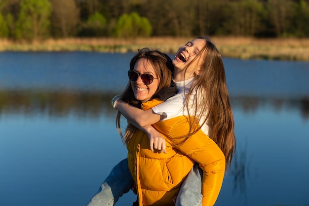 Madre juguetona dando a su hija un paseo a cuestas en la orilla del lago Spring