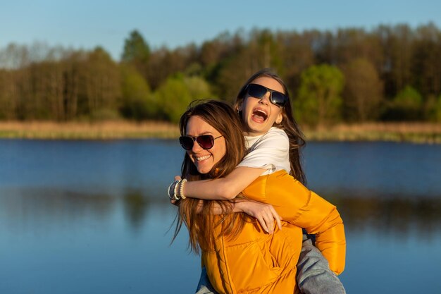 Madre juguetona dando a su hija un paseo a cuestas en la orilla del lago Spring