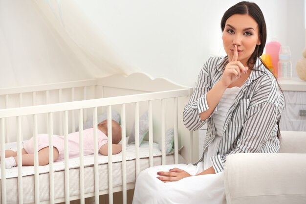 Foto madre junto a la cuna con bebé durmiendo en casa