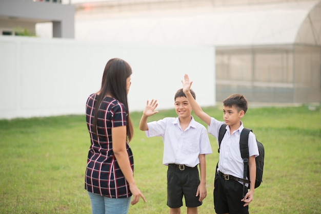 Madre llevando hijos a la escuela juntos, mano ola dice adiós