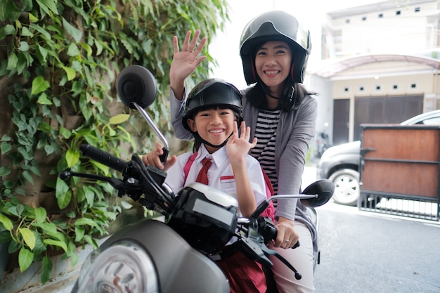 Madre llevando a su hija a la escuela en motocicleta por la mañana