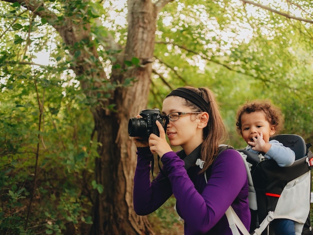 Madre llevando a su hijo en la espalda despertando en el bosque