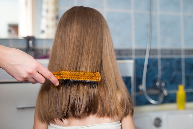 Madre mano con cepillo peinando el cabello largo de niña niño después del baño
