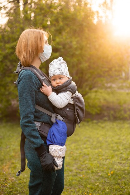 Madre con máscara médica con hijo pequeño jugando en el parque en sunsret