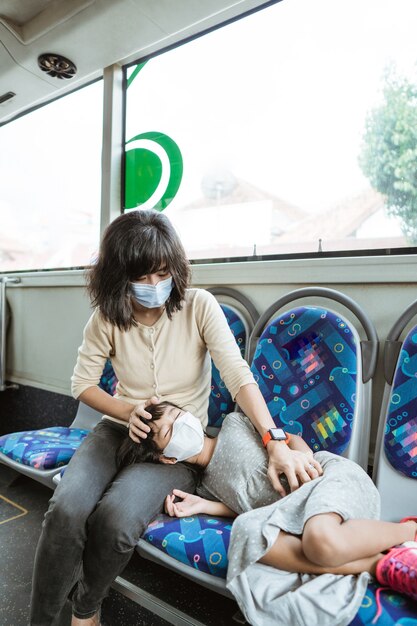 Una madre con una máscara y su hija duermen en un banco mientras viajan en autobús