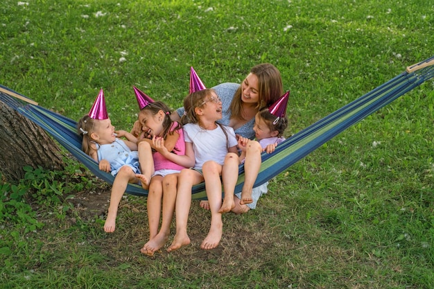 Madre mece a sus hijas en una hamaca en el parque y se ríe alegremente con ellas