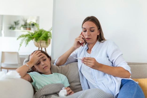 Madre midiendo la temperatura de su hijo enfermo. Niño enfermo con fiebre alta acostado en la cama y madre sosteniendo el termómetro. Madre con teléfono celular llamando al médico