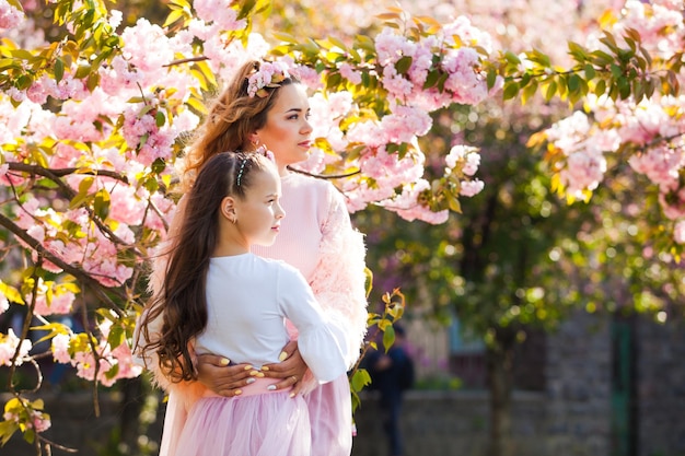 Madre de moda con hija caminando entre árboles de sakura. Moda femenina de primavera.