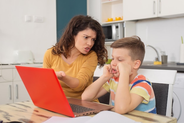 Madre molesta mirando a su hijo haciendo el tonto mientras hacía clases en línea