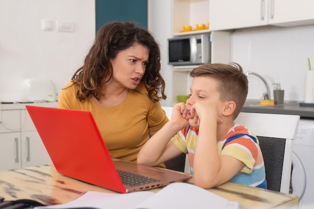 Madre molesta mirando a su hijo haciendo el tonto mientras hacía clases en línea