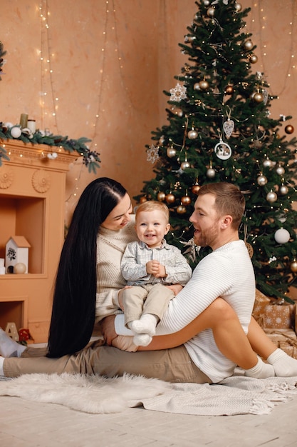 Madre morena padre e hijo pequeño sentados cerca del árbol de Navidad y jugando