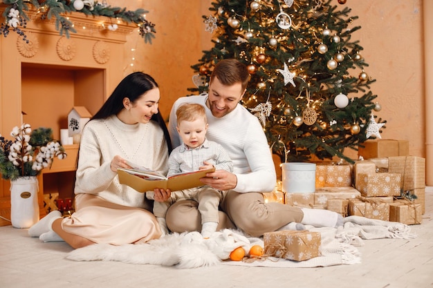 Madre morena padre e hijo pequeño sentados cerca del árbol de Navidad