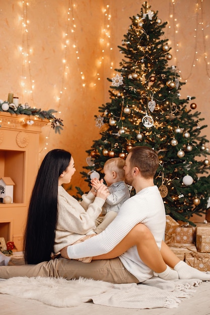 Madre morena padre e hijo pequeño sentados cerca del árbol de Navidad