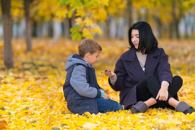 Una madre mostrando a su hijo algo en la mano en un parque entre hojas amarillas de otoño.