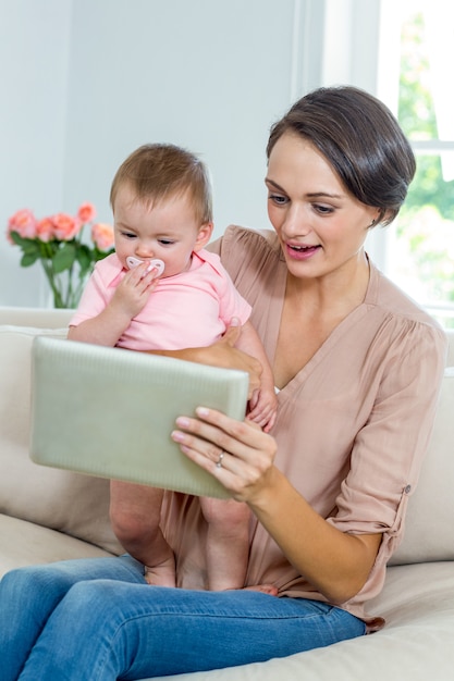 Madre mostrando tableta digital a hijo mientras está sentado en el sofá