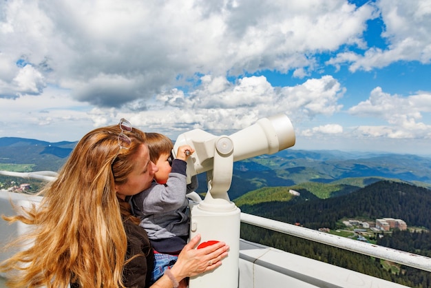 La madre muestra a su hijo paisajes en el valle de las montañas Ródope y el cielo a través del telescopio en la torre de observación de Snezhan