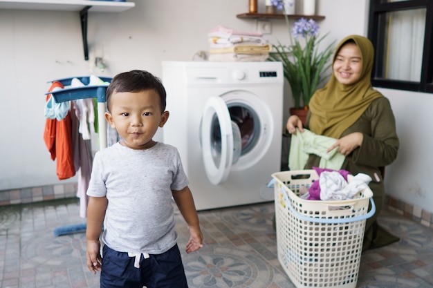 Madre musulmana ama de casa con un bebé en lavandería con lavadora